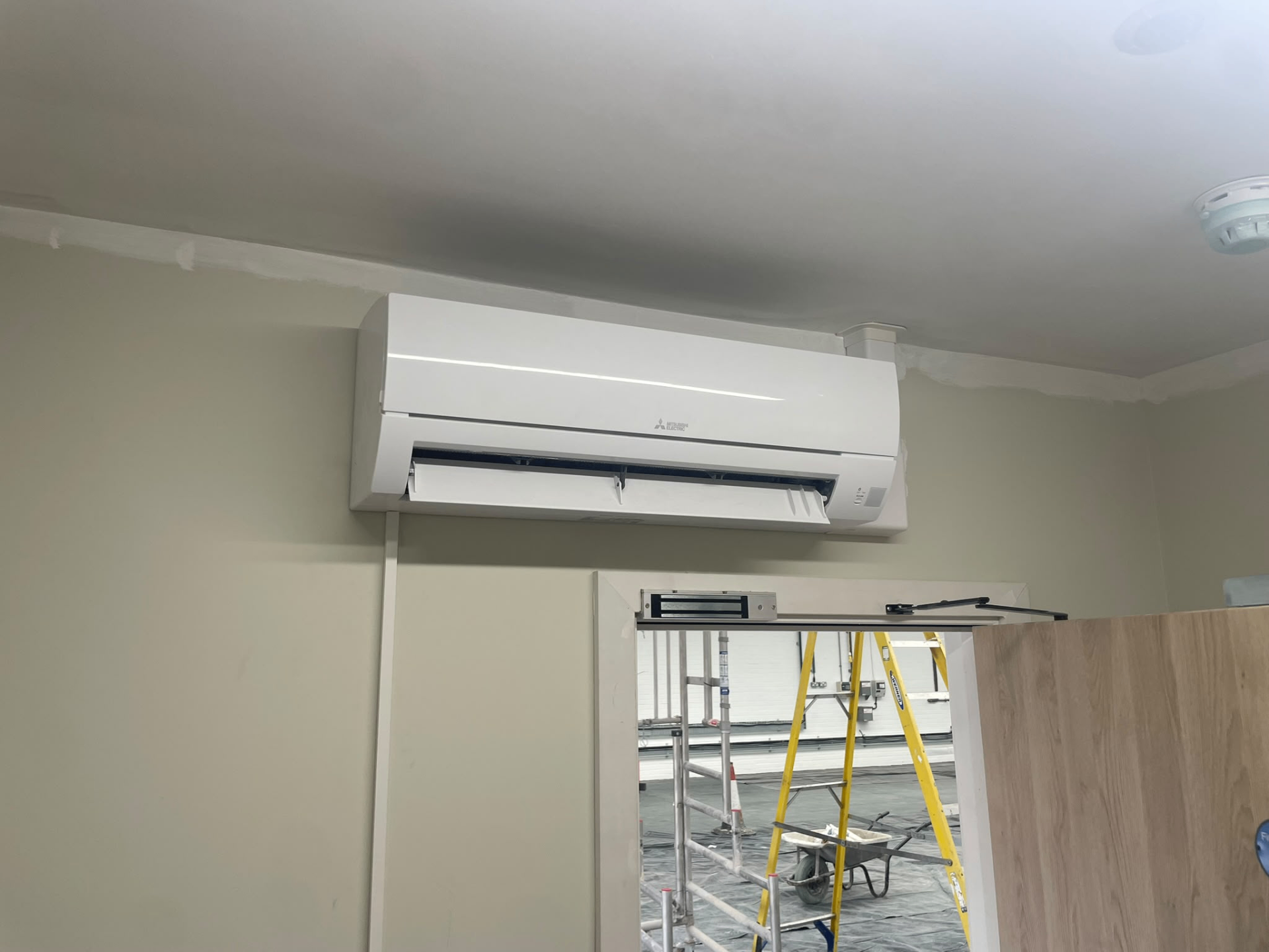 Mitsubishi Electric wall-mounted air conditioning unit installed high on a commercial interior wall by JC Heating and Cooling.