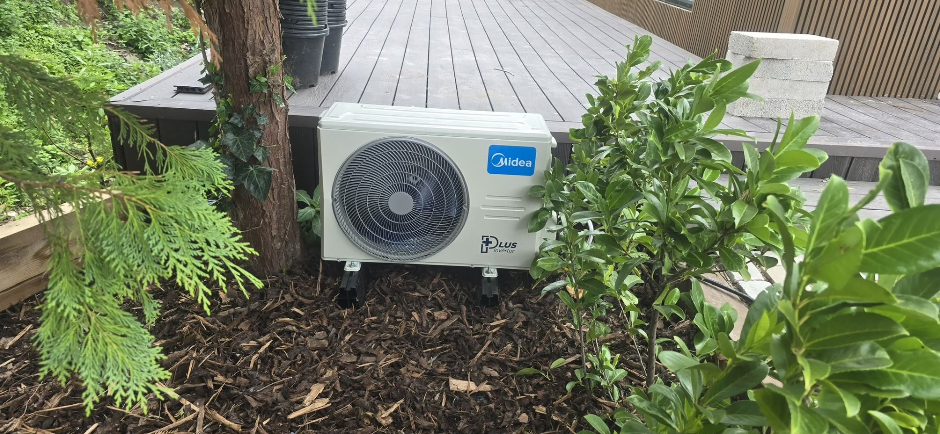 Midea air-source heat pump installed on a residential garden plinth in Greater Manchester.